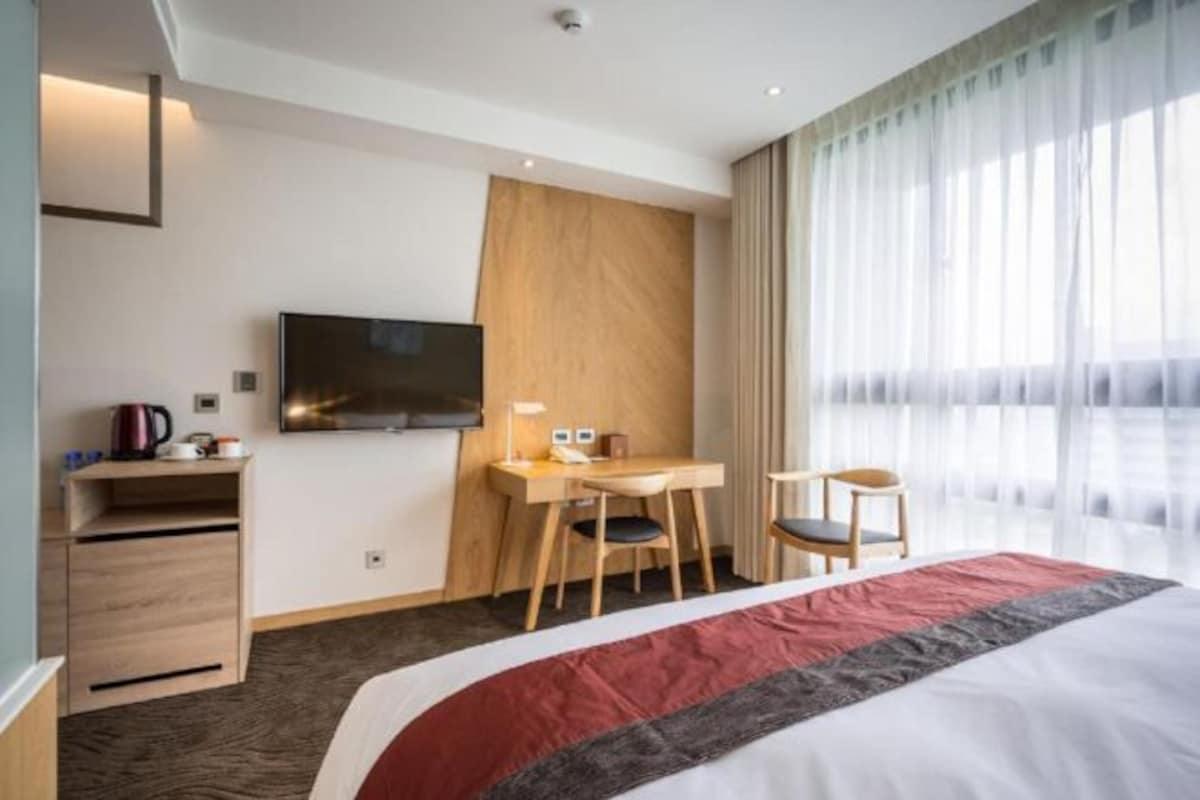 A hotel room with a bed, a desk, a chair, a television, and a window with curtains.