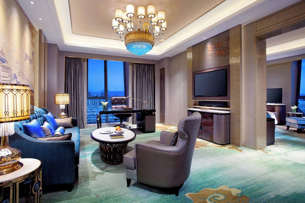 Habitación de hotel moderna con vista a la ciudad, un gran candelabro, televisor de pantalla plana y una zona de estar confortable.