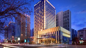Un hotel moderno con un llamativo letrero WandaVista, rodeado de edificios altos y una calle concurrida al anochecer.