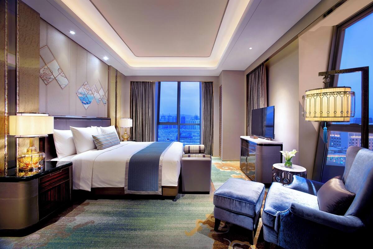 Una habitación de hotel moderna con una cama grande, un área de descanso, un televisor y vistas a la ciudad.