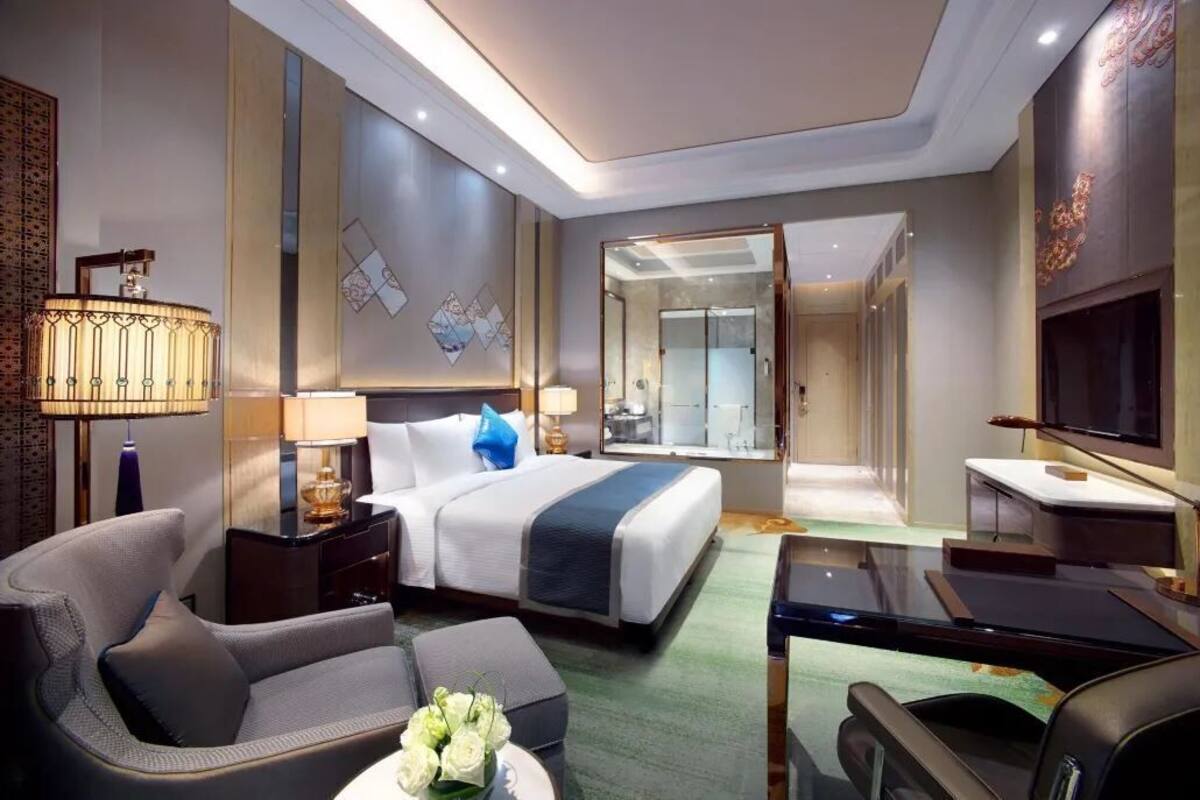 Una habitación de hotel moderna con cama, escritorio, silla, televisor y un baño visible a través de una puerta abierta.
