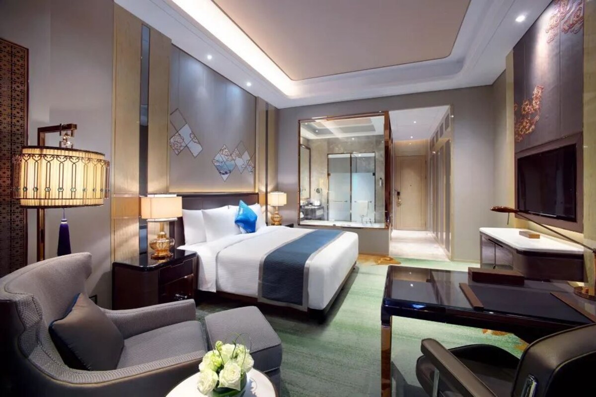 Una habitación de hotel moderna con cama, escritorio, silla, televisor y un baño visible a través de una puerta abierta.