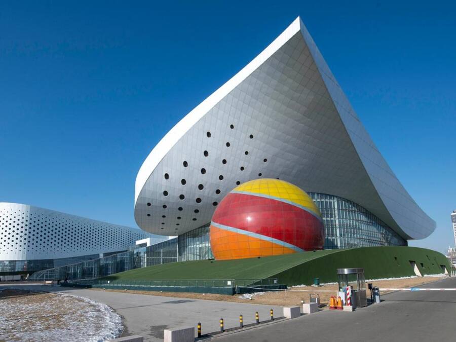 A modern building with a unique curved roof and a large spherical sculpture.