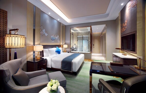 A modern hotel room with a large bed, a sitting area with a sofa and armchair, a desk with a chair, and a television. - Wanda Vista Hohhot (Hohhot)
