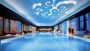 Una piscina interior con diseño moderno, que presenta una gran obra de arte iluminada en el techo y sillones de descanso a lo largo de los bordes.