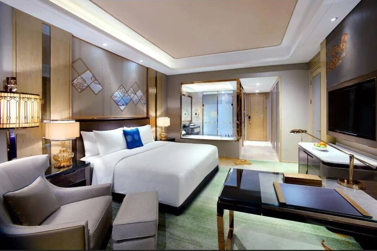 Habitación de hotel con cama, escritorio, televisión, lámpara y vistas al exterior.