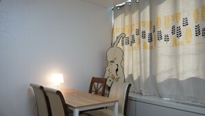 A dining area with a table and chairs, a window with a curtain, and a wall-mounted lamp. - Hongstay in Hongdae (Seoul)
