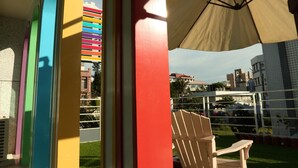 Un patio con un arco de colores, una sombrilla color beige y una silla de madera.
