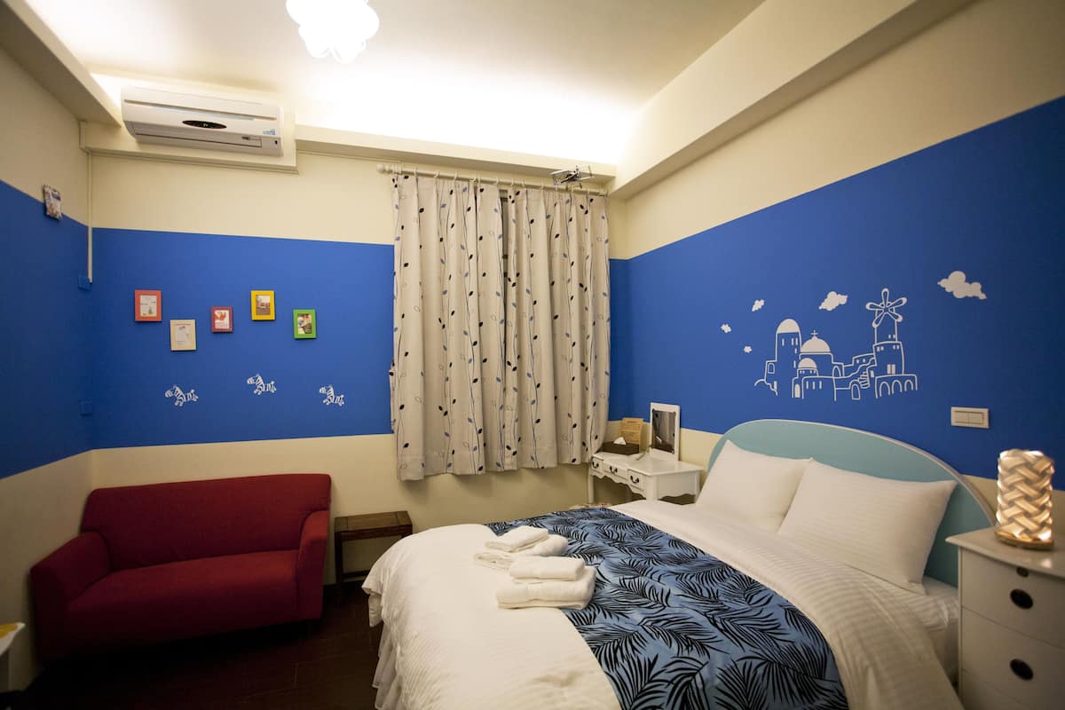 A hotel room with a bed, a red sofa, a nightstand, and a wall with decorative stickers.