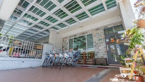 Un edificio moderno con fachada de vidrio, una estación de alquiler de bicicletas y una planta en maceta.