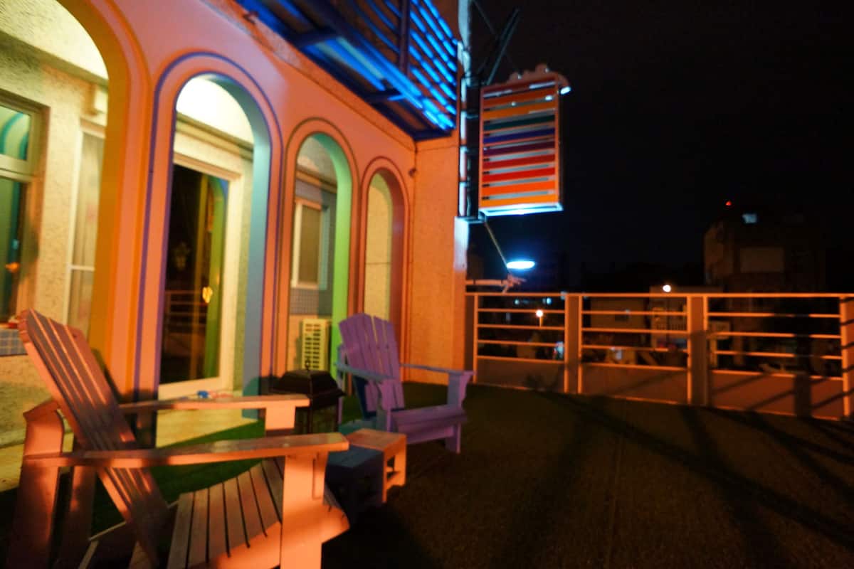An outdoor deck with chairs and tables, a railing, and a building with arched windows.
