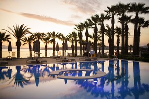 A pool area with lounge chairs and umbrellas, surrounded by palm trees. - Boyalık Beach Hotel & SPA Thermal Resort  (Cesme)