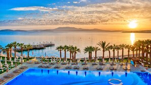 A resort pool with lounge chairs and umbrellas, overlooking a calm body of water and mountains during sunset. - Boyalık Beach Hotel & SPA Thermal Resort  (Cesme)
