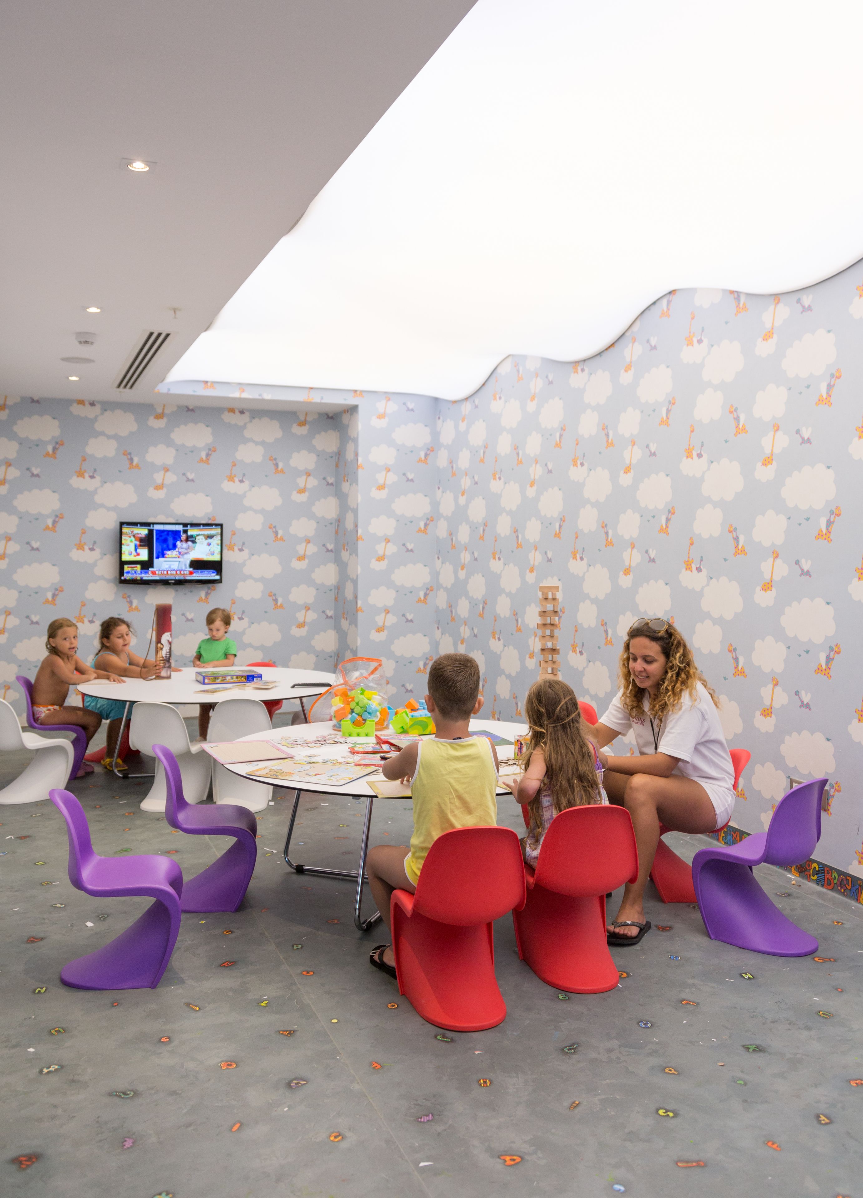 A children's playroom with a round table, colorful chairs, and a wall-mounted TV.