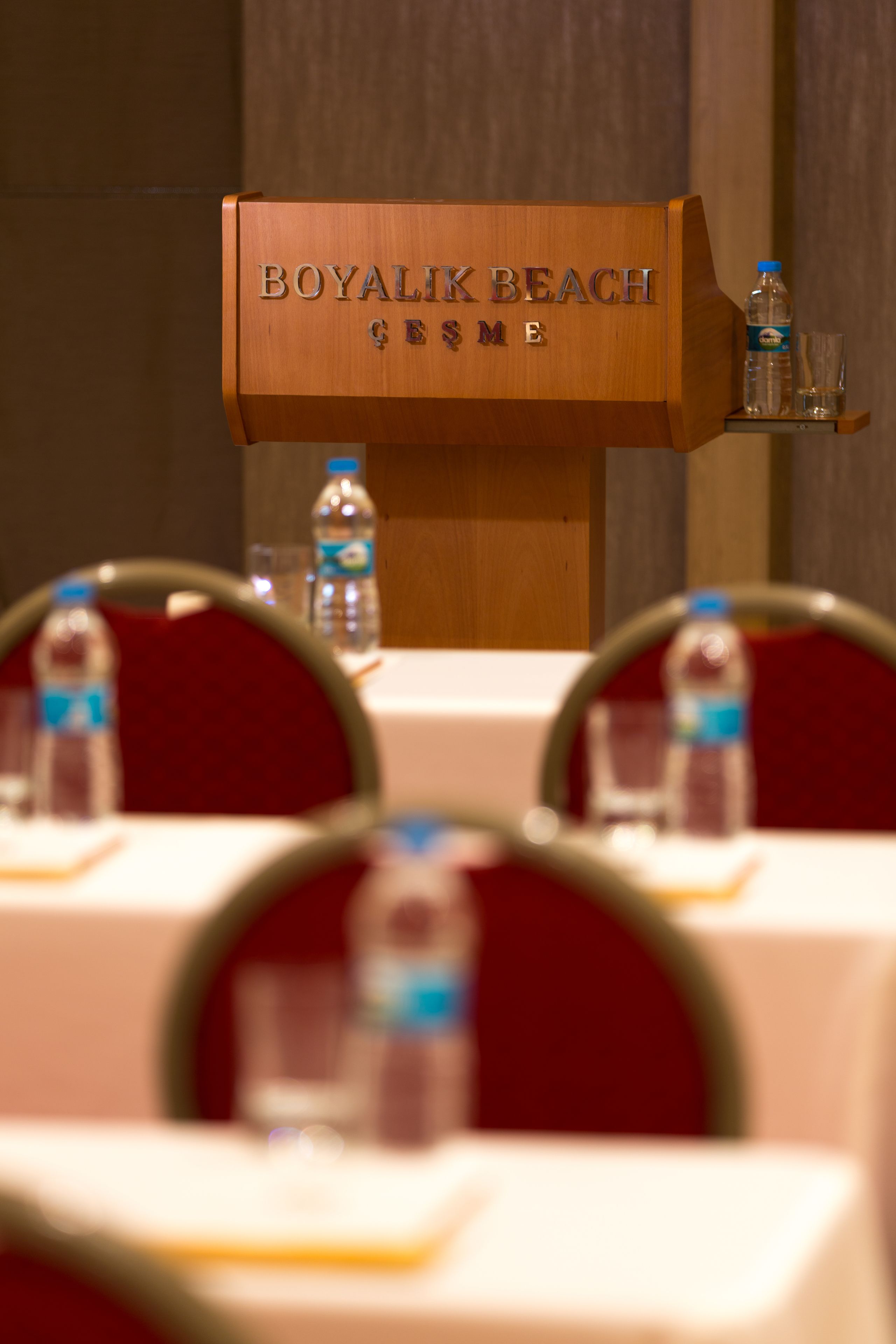 Ein hölzernes Rednerpult mit der Aufschrift "BOYALIK BEACH", platziert auf einem Tisch mit Wasserflaschen und Gläsern.