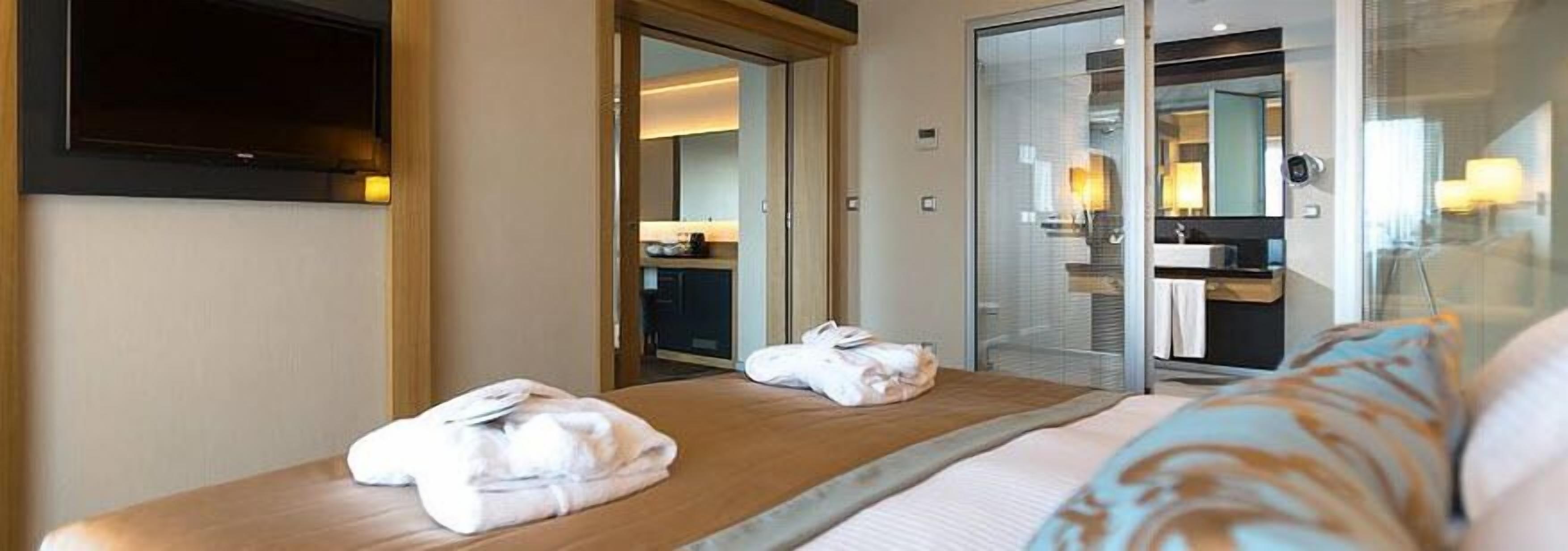A hotel room with a bed, a bathroom with a glass shower, and a view of the outside.