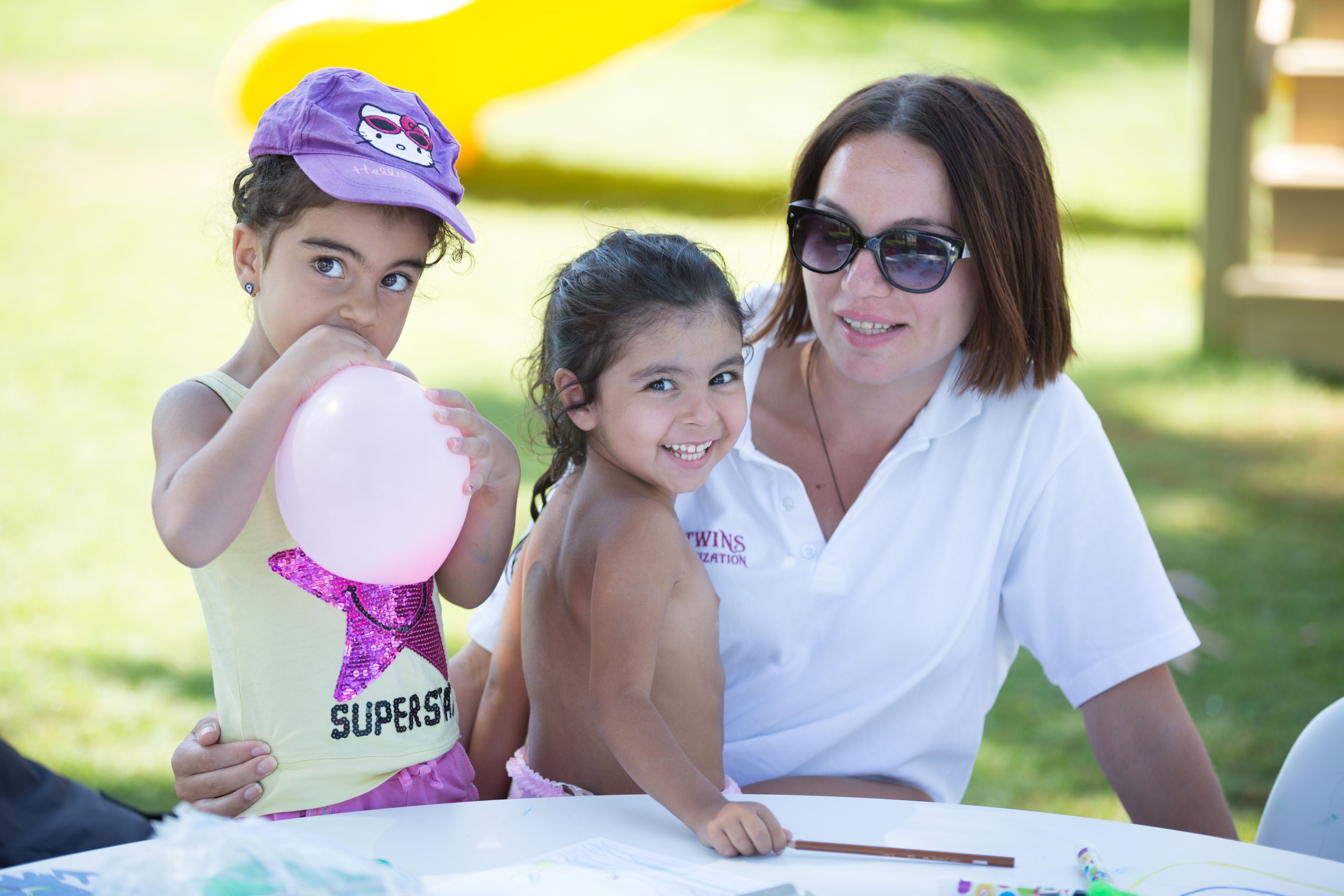 A woman and two children at a table with a yellow slide in the background.