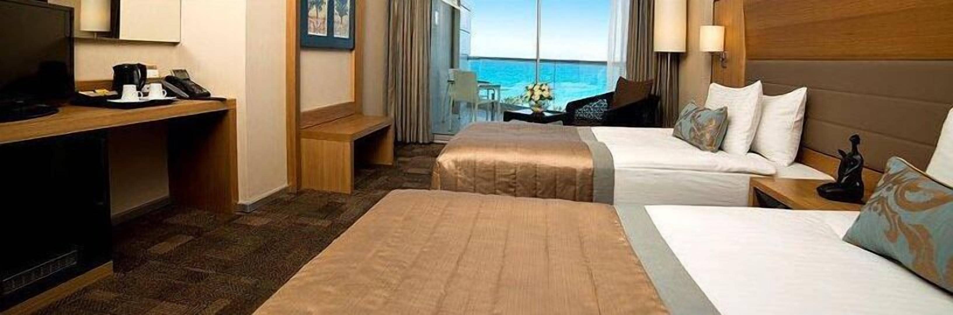 A hotel room with two beds, a desk with a phone and coffee maker, a chair, and a view of the ocean.
