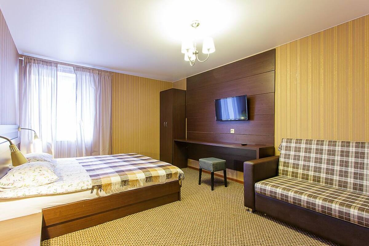 A hotel room with a bed, a sofa, a TV mounted on the wall, and a small table.