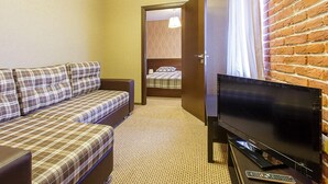 A hotel room with a sofa, a TV, and a brick wall.