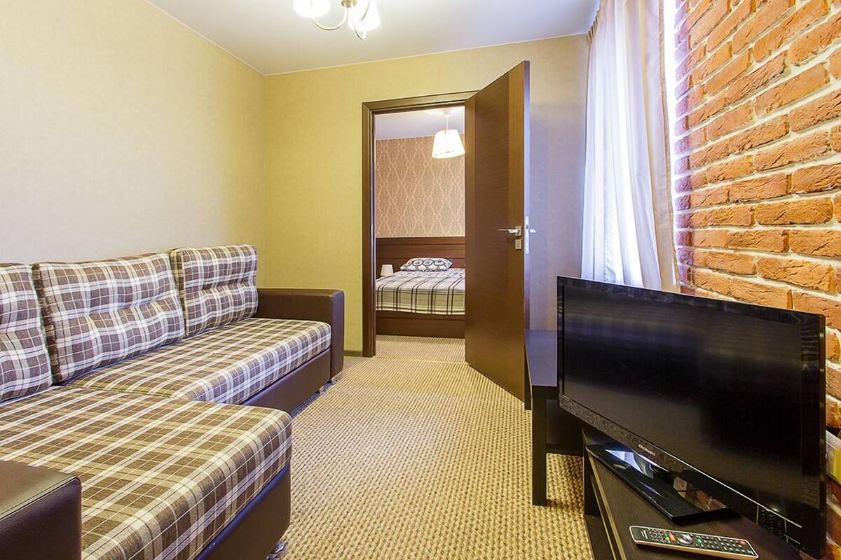 A hotel room with a sofa, a TV, and a brick wall.