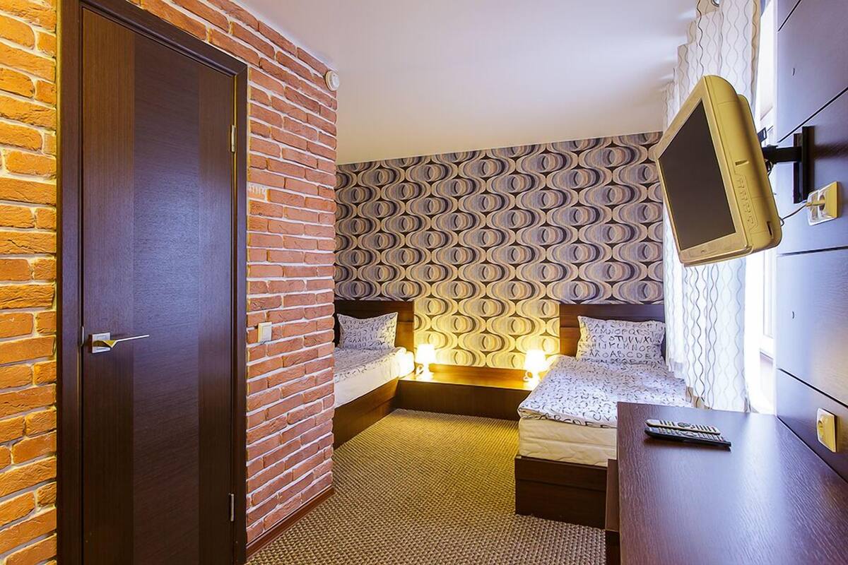 A hotel room with a brick wall, two beds, a TV, and a desk.