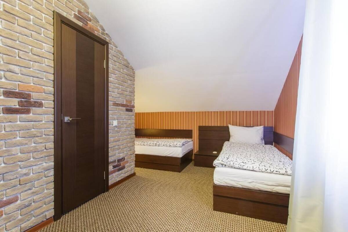 A bedroom with two beds, a brick wall, and a wooden ceiling.