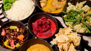 Una mesa con varios platos que incluyen arroz, curry de pollo, remolachas, judías verdes y un tazón de lentejas.