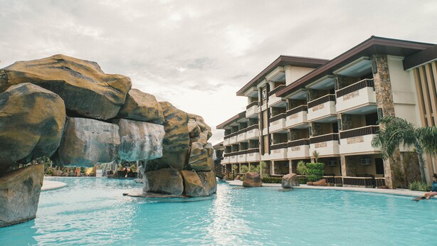 A hotel with a pool area featuring large rock formations and a multi-story building with balconies. - Cebu Westown Lagoon - South Wing (Mandaue)
