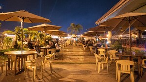 An outdoor dining area with tables and chairs under umbrellas, palm trees, and a paved walkway. - Cebu Westown Lagoon - South Wing (Mandaue)