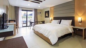 A hotel room with a large bed, a desk with a chair, a TV, and a view of the outside. - Cebu Westown Lagoon - South Wing (Mandaue)
