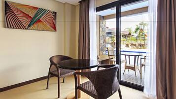 A room with a dining table and chairs, a large window with curtains, and a colorful abstract painting on the wall.