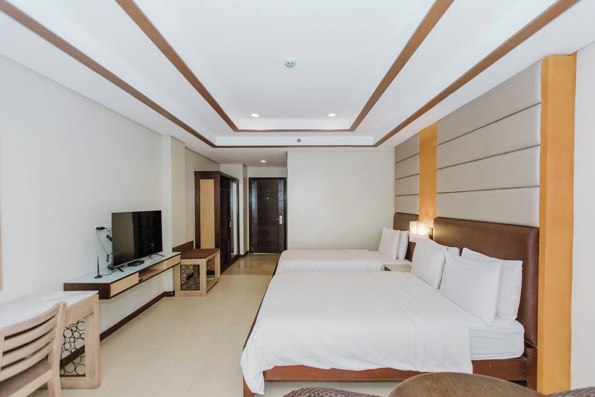 Ein Hotelzimmer mit einem großen Bett, einem Fernseher, einem Schreibtisch und einem Kleiderschrank.