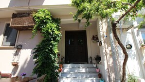 A building with a staircase leading to a dark door, surrounded by potted plants and outdoor furniture. - Oyku Butik Otel (Bozcaada)