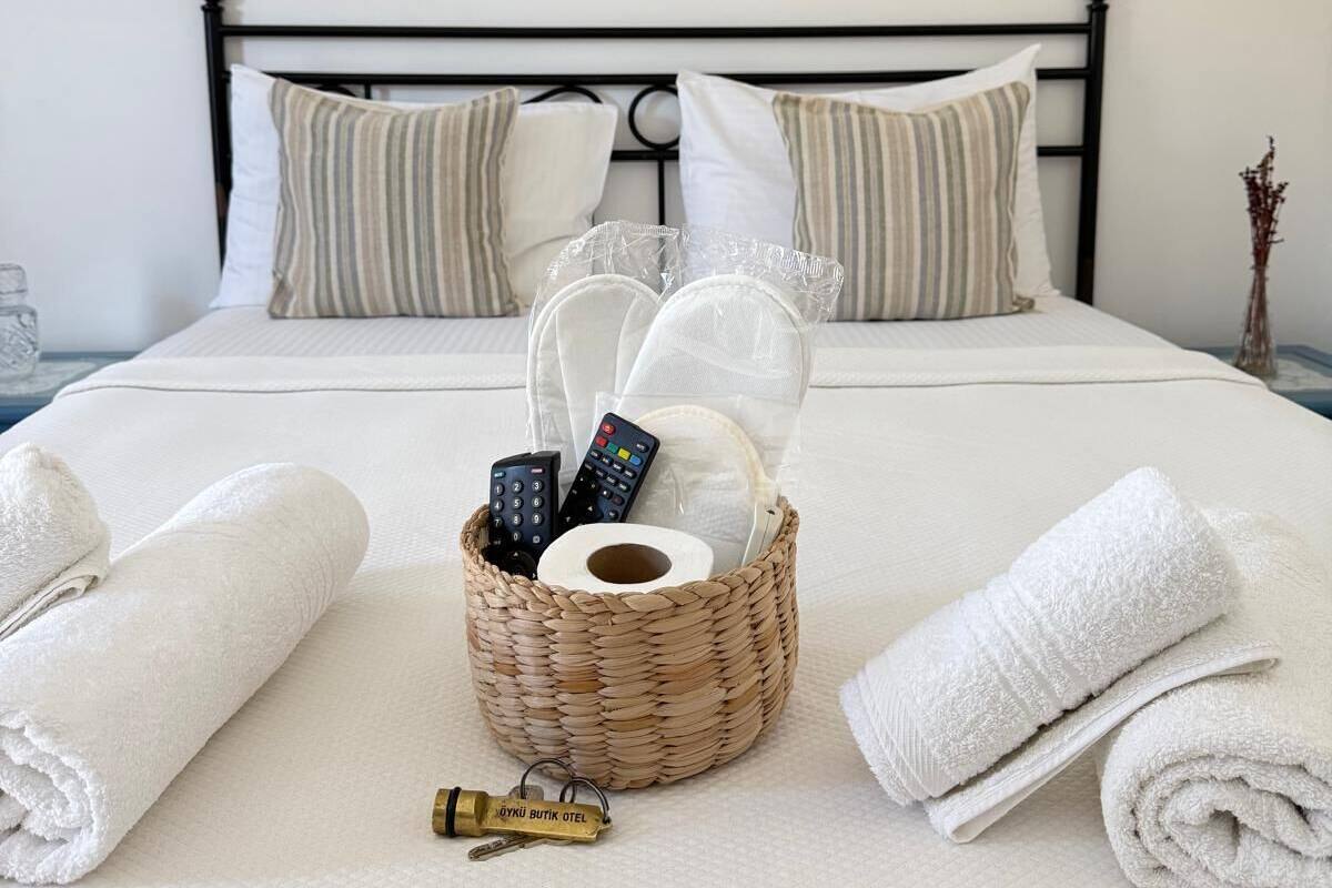 A neatly made bed with white linens, a basket of toiletries, and a framed picture on the wall.