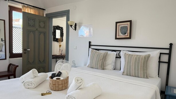 A neatly made bed with rolled towels, a wicker basket with toiletries, and a framed picture on the wall. - Oyku Butik Otel (Bozcaada)