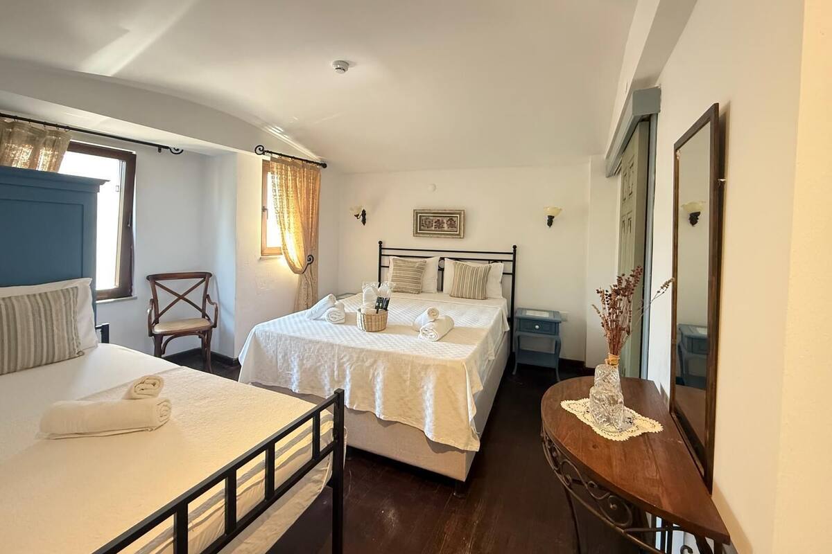 A bedroom with two beds, a desk, a chair, a window with curtains, and a mirror.