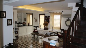 A dining area with a table set for four, a kitchen in the background, and a staircase leading to another floor. - Oyku Butik Otel (Bozcaada)