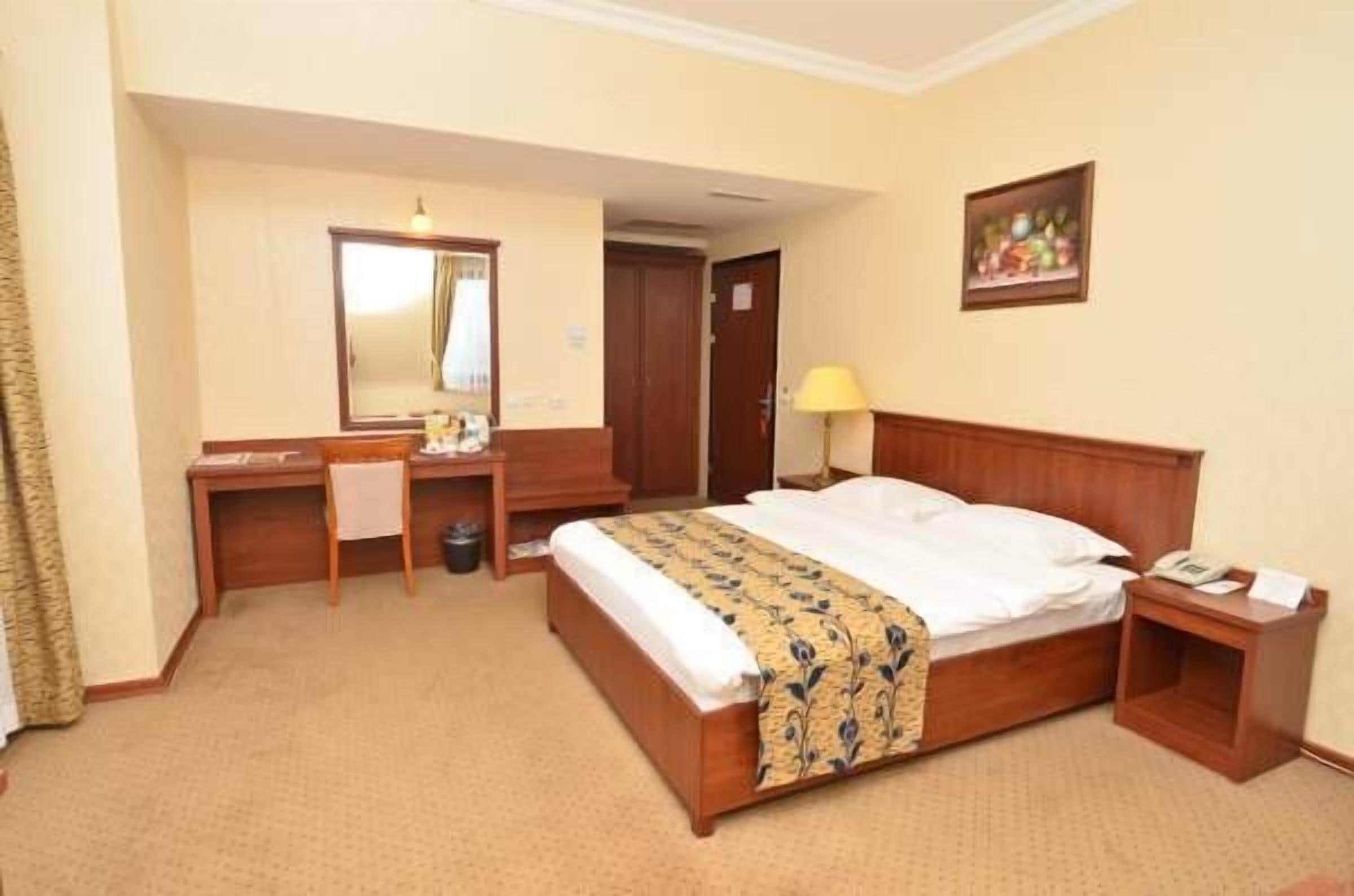 Una habitación de hotel con una cama de madera, un escritorio, una silla, una mesita de noche, una lámpara y un cuadro en la pared.