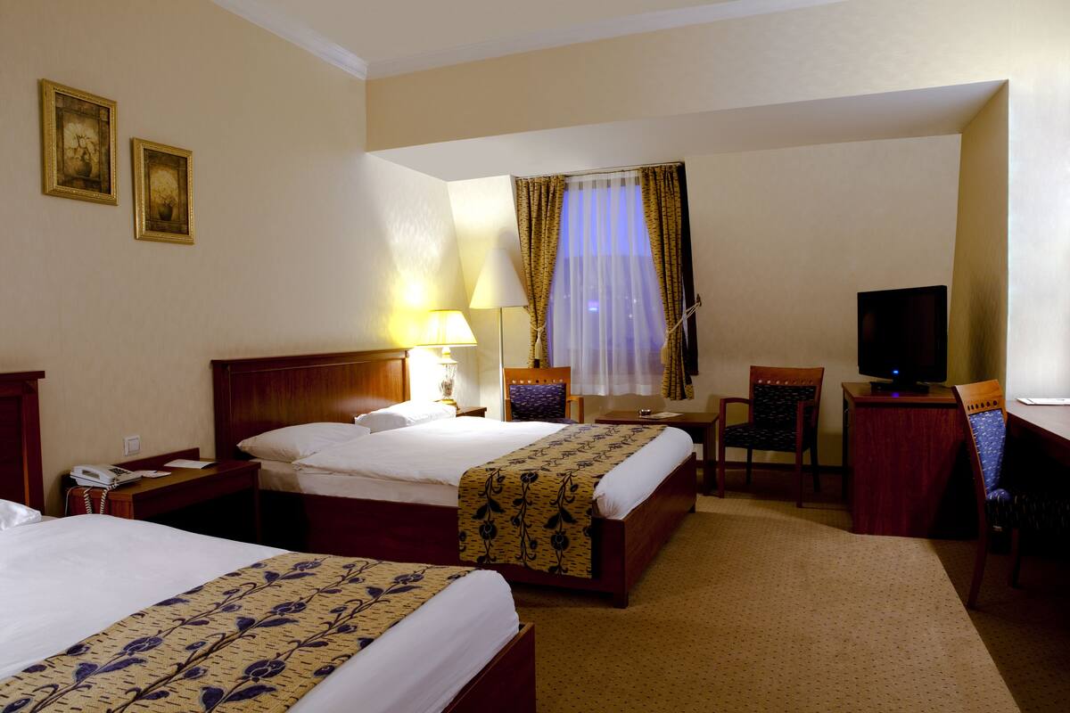 Une chambre d’hôtel avec deux lits, un bureau, une chaise, une télévision et une lampe.