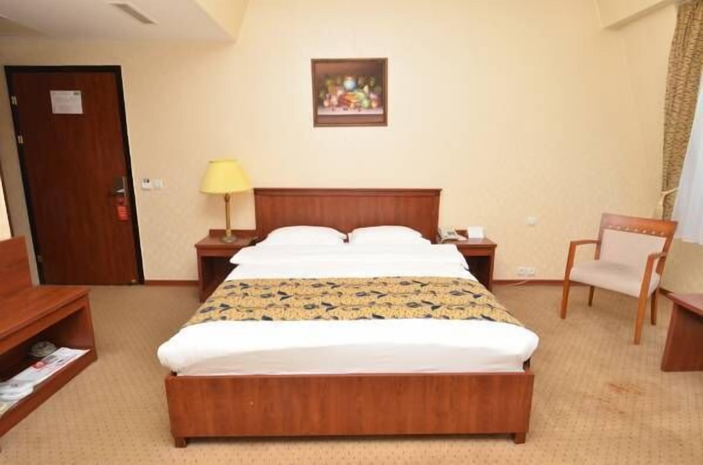 Een hotelkamer met een houten bed, een nachtkastje, een stoel en een schilderij aan de muur.