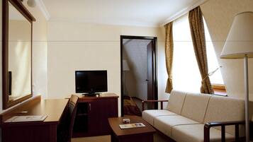 A hotel room with a television, a sofa, a desk, and a lamp.