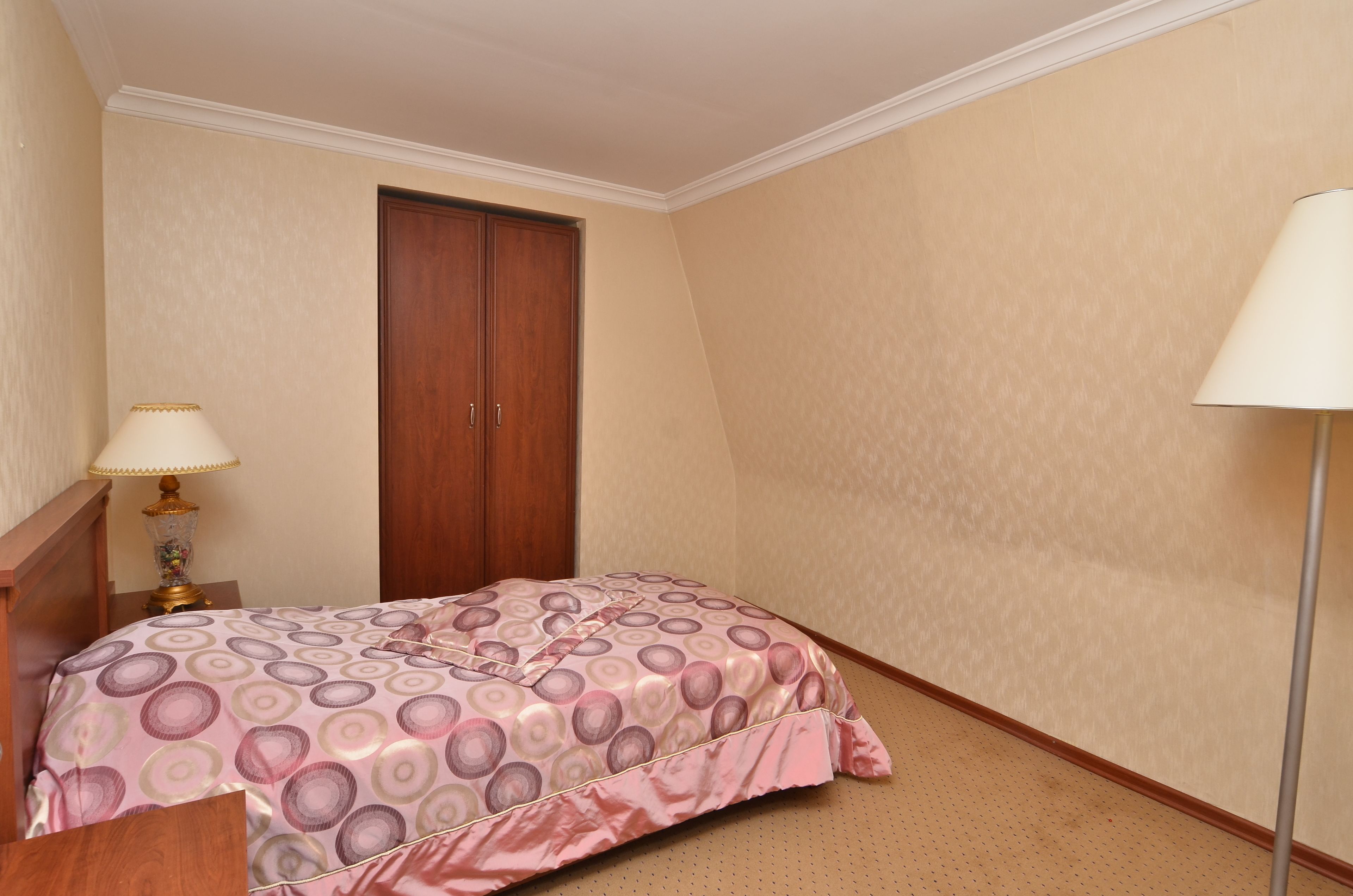A bedroom with a bed, a nightstand, a lamp, and a wardrobe.