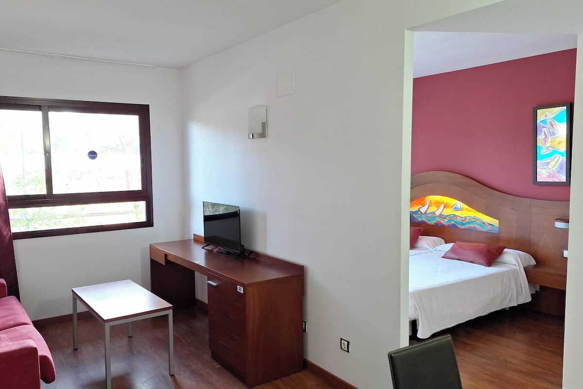 A hotel room with a bed, a desk, a chair, a TV, and a window with curtains.