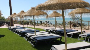 Un área de descanso en la playa con sombrillas de paja y tumbonas dispuestas en filas.