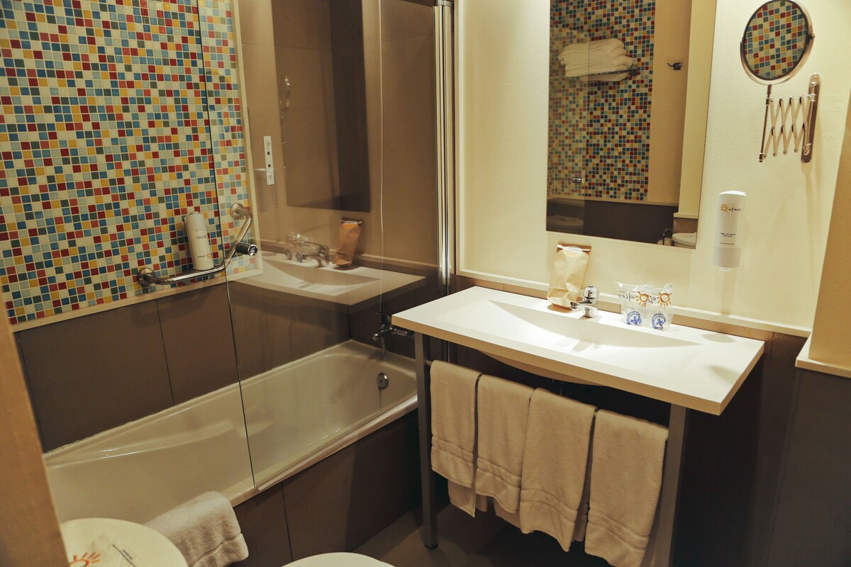 A bathroom with a mosaic tile wall, a bathtub, a sink, and a mirror.