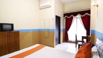 Habitación de hotel con una cama, un televisor sobre un mueble de madera, un espejo, una puerta y una ventana con cortinas rojas.