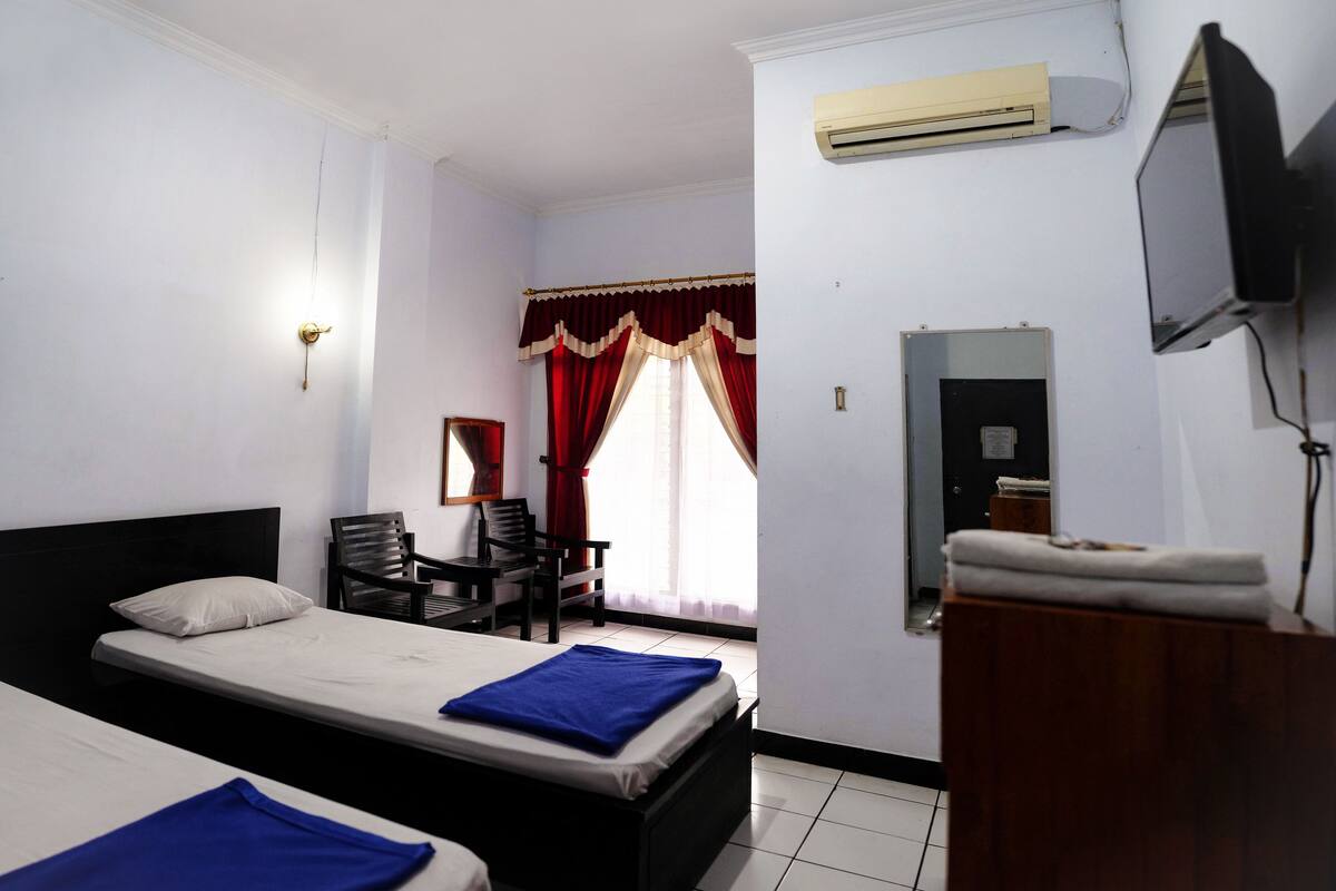 A hotel room with two beds, a desk, a chair, an air conditioning unit, and a television.