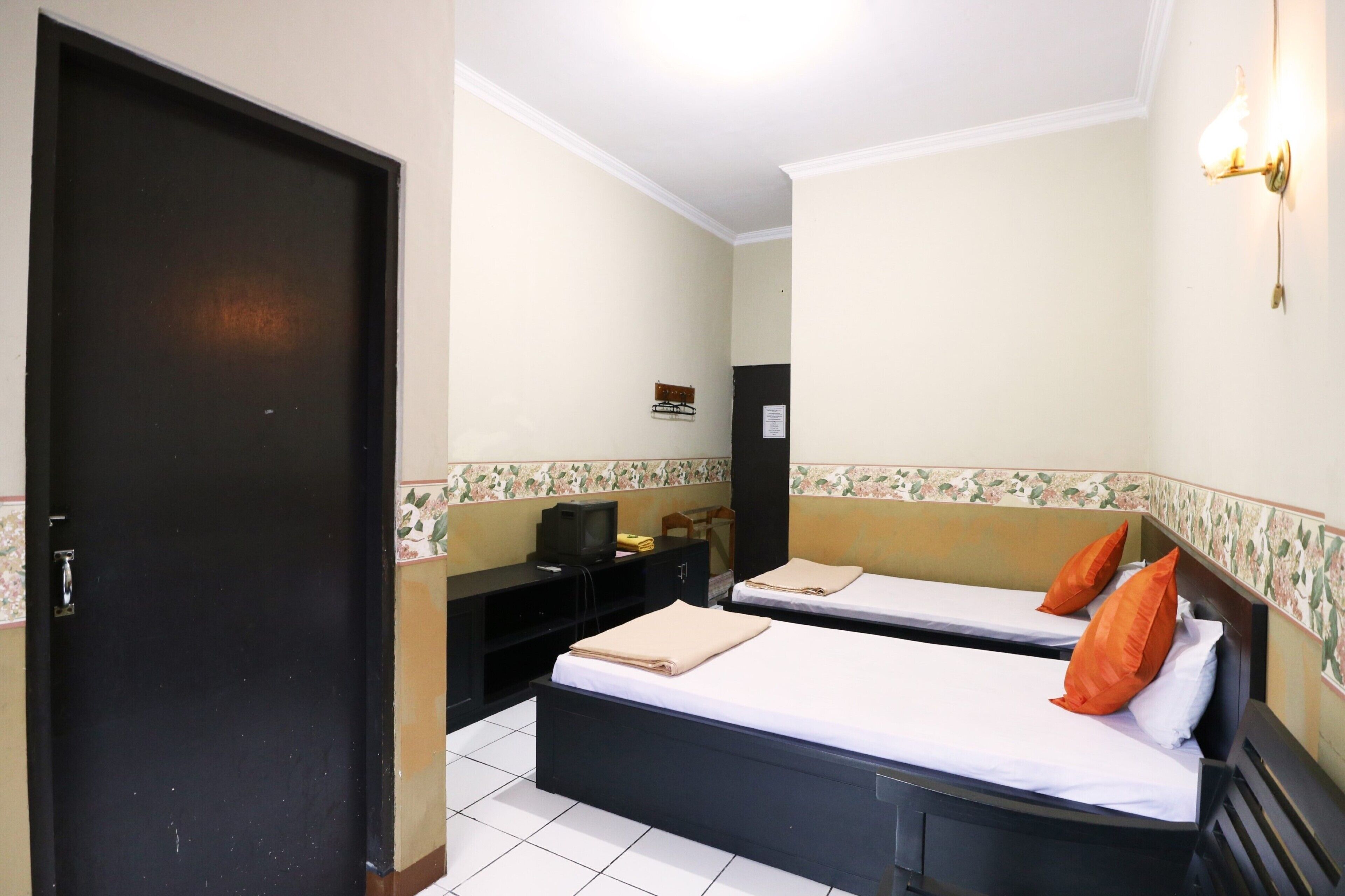 Ein Hotelzimmer mit zwei Betten, einem Schreibtisch, einem Fernseher und einer Tür.