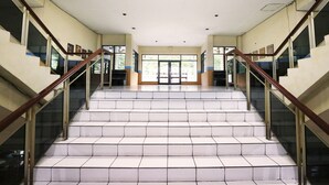 Una escalera con barandillas de cristal y baldosas blancas que conduce a un espacio interior luminoso con ventanas grandes.